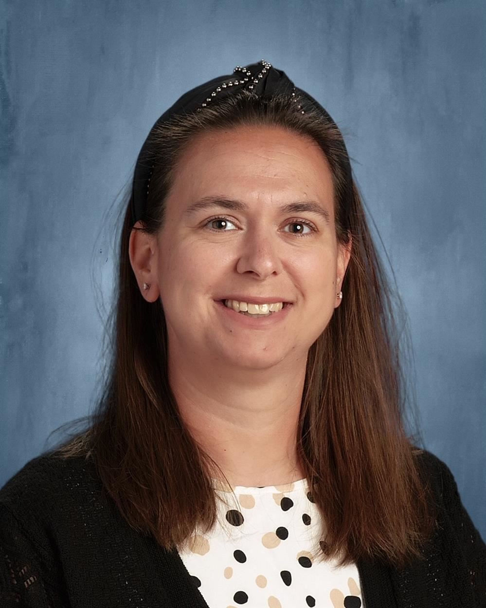 Picture of woman with white dress and black headband. Brown hair to shoulders and brown eyes.